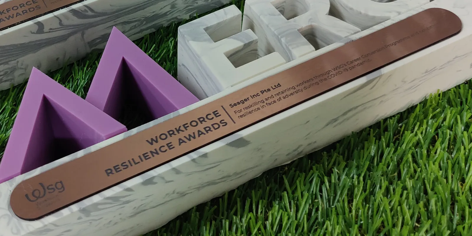 Close-up of an engraved brass plate reading WORKFORCE RESILIENCE AWARDS beside the WSG logo, the winner's name and the citation, set into a marbled base