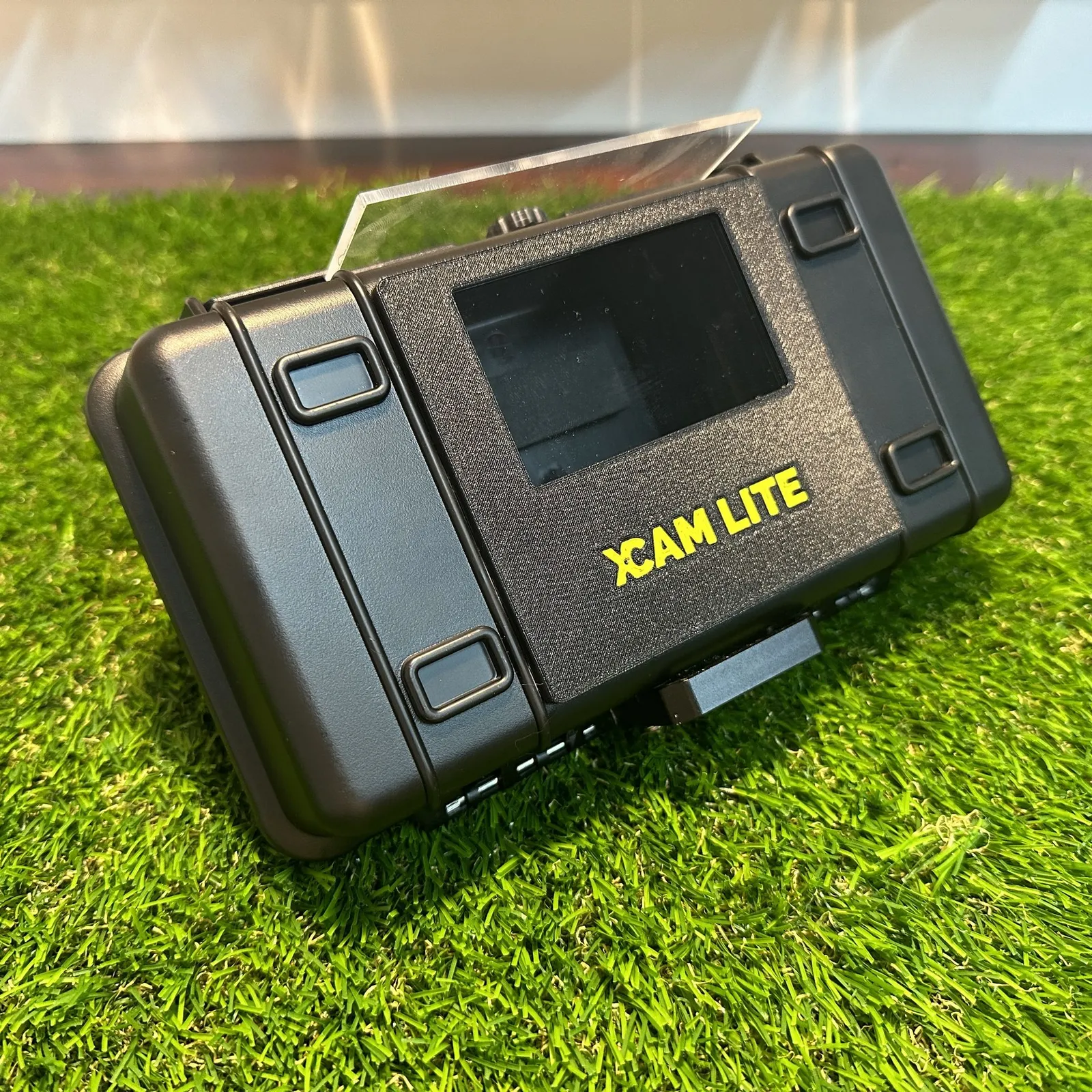 A single finished housing standing on its end, the XCAM LITE front panel facing forward and the clear cover raised