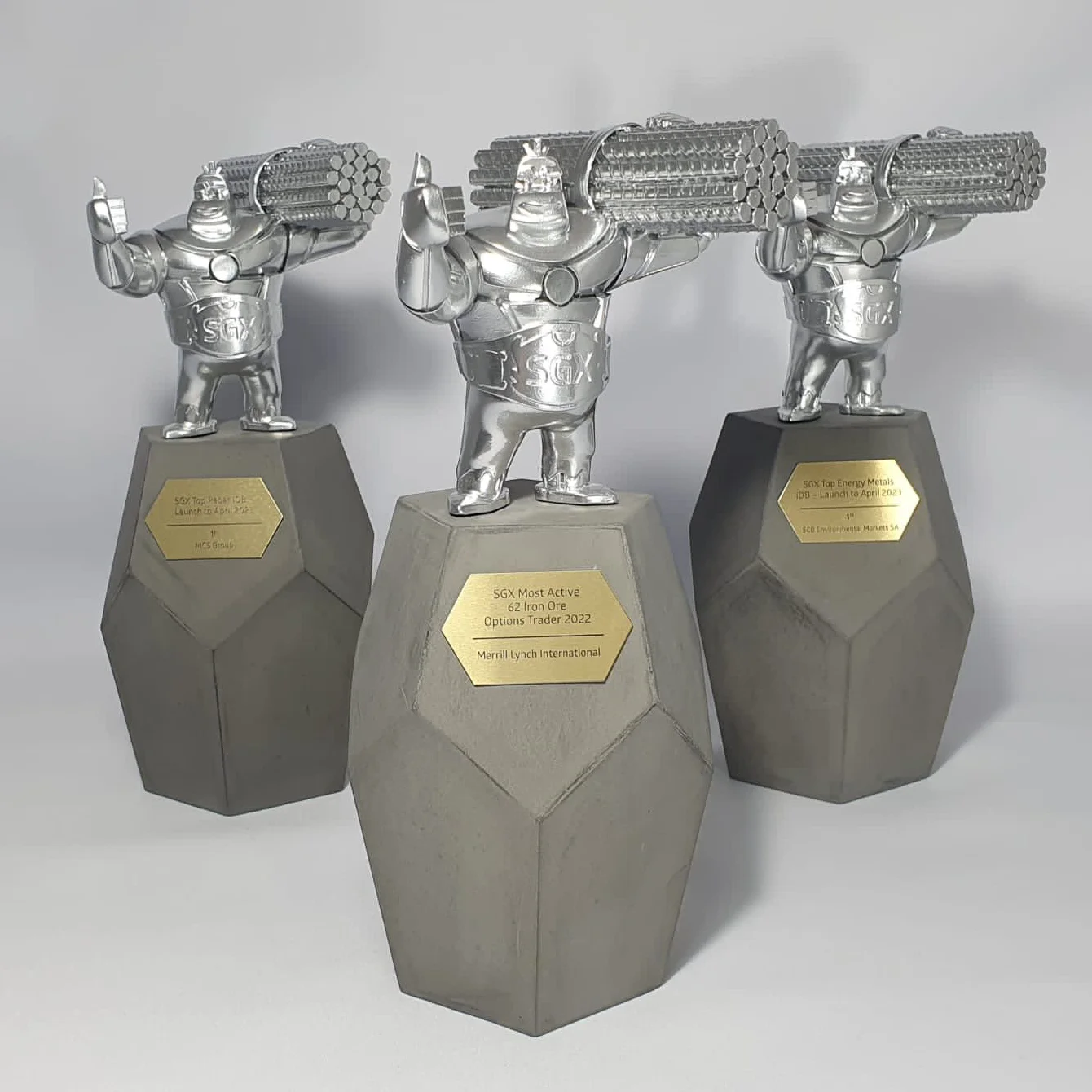 Matched set of three silver sculptural figure awards on faceted concrete-grey bases with gold SGX plaques