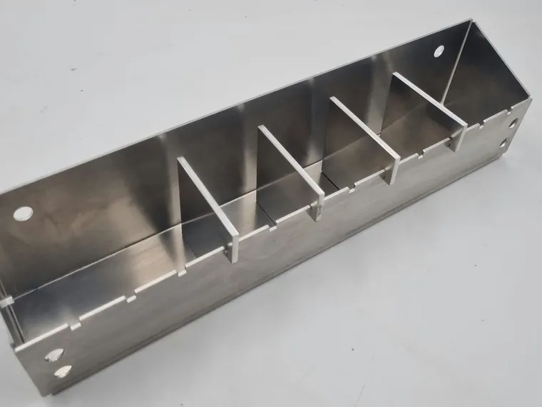 A long aluminium tray bent from sheet, with four flat dividers slotted into a row of notches cut along one side, and round mounting holes at each end