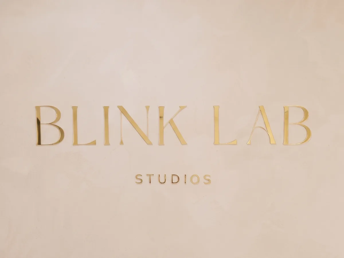 Polished gold Blink Lab Studios lettering on a plaster wall