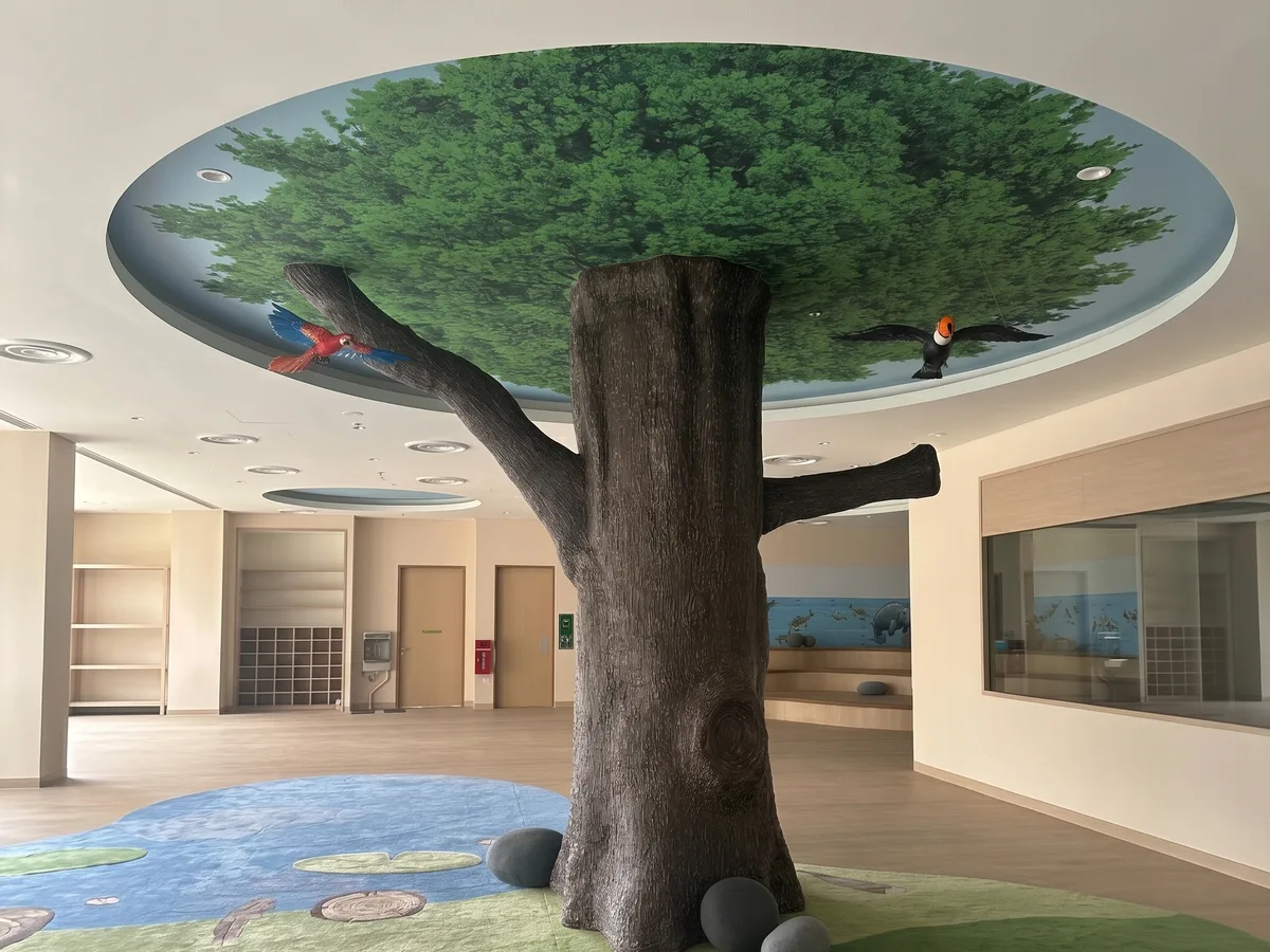 Printed rainforest canopy ceiling mural with sculpted tree pillar at Mandai Zoo kindergarten
