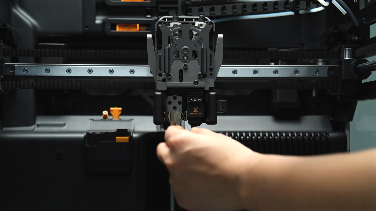 A hand releasing the hotend from the toolhead of a Bambu Lab H2 series printer