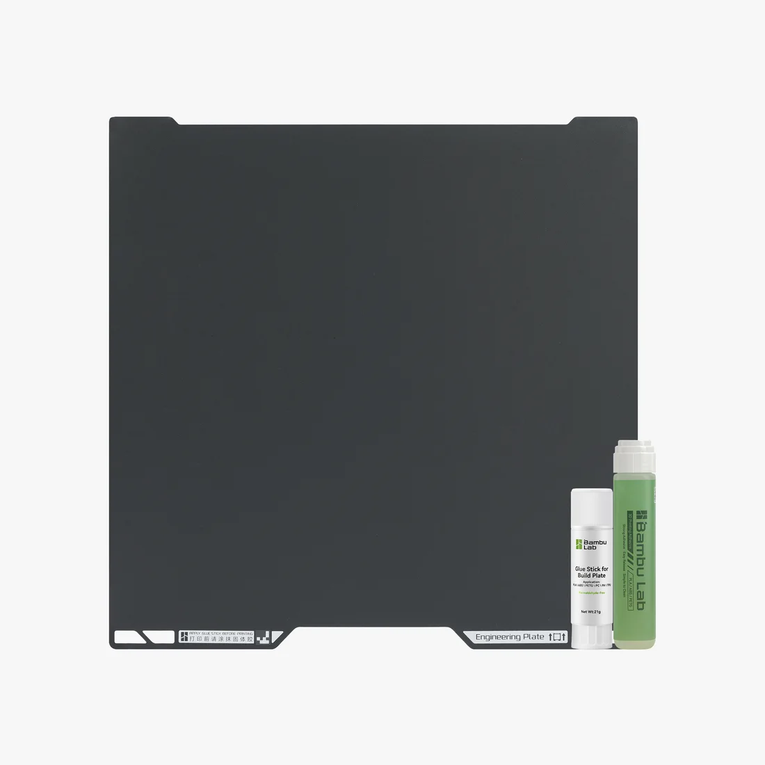 The matte black engineering plate photographed with a Bambu glue stick and a bottle of liquid adhesive.