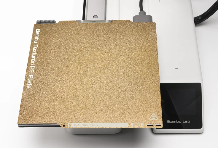 The gold textured PEI plate seated on the heatbed of a Bambu printer.